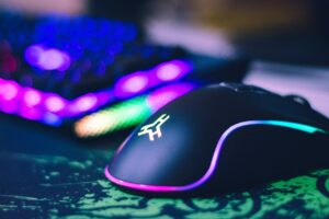 Eine bunt beleuchtete Gaming Maus liegt neben einer ebenfalls beleuchteten Tastatur