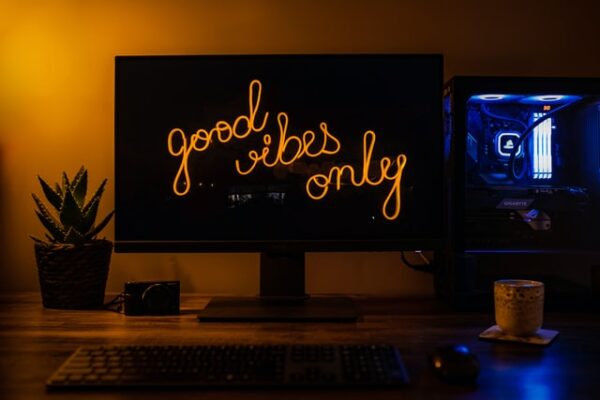 Hinter einem Desktop mit dem Bildschirmschoner "Good Vibes Only" hinter dem ein beleuchteter PC steht