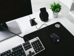 Auf einem Schreibtisch steht ein PC-Bildschirm, eine Tastatur und eine Gaming-Maus auf einem Mauspad