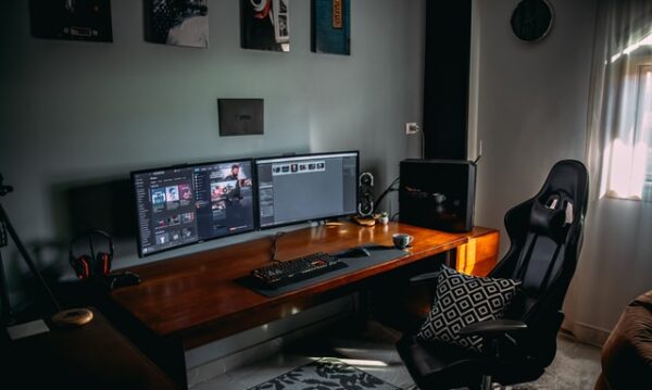 Ein Gaming-Setup bestehend aus zwei Bildschirmen, einer beleuchteten Tastatur und Maus, einer Mausmatte und einem Gaming-Chair.