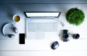 Die Draufsicht eines Laptops, neben dem eine Kamera, Maus, Kopfhörer, ein Handy, eine Pflanze und eine Tasse stehen