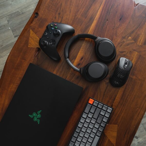 Auf einem Holztisch liegt ein Laptop, eine Maus, Tastatur, ein Kontroller und Kopfhörer