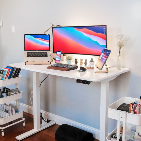 Ein weißer, höhenverstellbarer Tisch auf dem Laptop, Tablet und PC stehen
