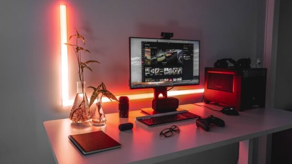 Hinter einem einfachen Tisch, auf dem ein Computer und Zubehör stehen, befindet sich eine rote Leuchtröhre
