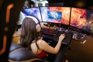 Eine Frau sitzt vor drei Monitoren und spielt ein PC-Game