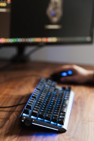 Person bedient eine leuchtende Tastatur und Maus, Bildschirm im Hintergrund