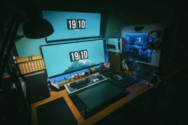 Ein Schreibstisch mit PC-Glasgehäuse, zwei Bildschirmen, die bläulich leuchten, Tastatur und kleinen Dekofiguren