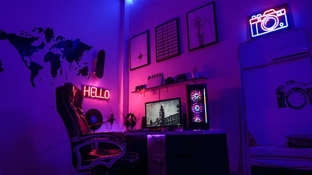 Ein in lila und pinkes Licht getauchter Arbeitsplatz mit Neonschildern an der Wand