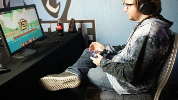 Ein Mann sitzt entspannt mit überschlagenen Beinen vor einem Bildschirm und spielt ein Spiel mit Controller