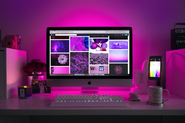 Ein pink beleuchteter Schreibtisch mit ergonomischer Gamingmaus, Handyhalterung, Tasse und Dekoration