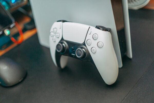 Ein weißer PS5-Controller, der an einer PlayStation-Konsole lehnt