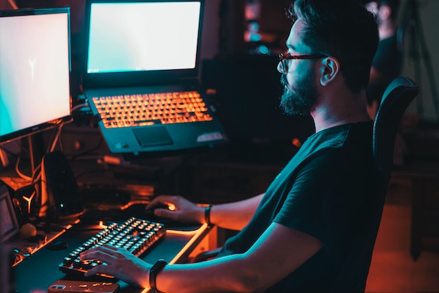 Ein Mann mit Headset sitzt an einem Schreibtisch mit mehreren Bildschirmen und spielt ein Computerspiel