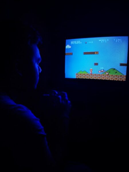 Ein Mann mit Controller sitzt ganz nah vor einem Fernseher, auf dem er Super Mario spielt