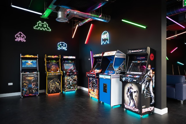 Eine dunkle Arcade-Halle mit mehreren Maschinen unterschiedlicher Gaming-Genre, die in bunten Farben aufleuchten